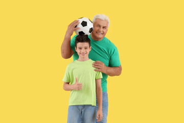 Canvas Print - Little boy with his grandfather holding soccer ball on yellow background