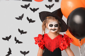 Poster - Little girl dressed for Halloween as witch with balloons and paper bats on light wall