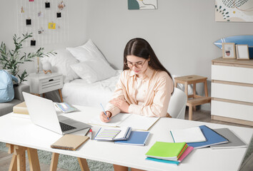 Canvas Print - Female student studying with notebooks and laptop at table in bedroom