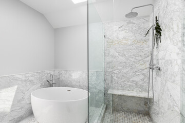 Wall Mural - A bathroom with a shower with marble tiles and eucalyptus hanging from the chrome showerhead. A round freestanding soaking tub sits on marble tiles with a chrome faucet.