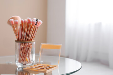 Wall Mural - Holder with makeup brushes and palette of eyeshadows on table at home