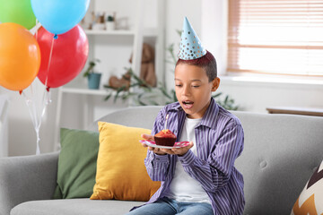 Sticker - Cute little African-American boy in party hat with birthday cake sitting on sofa in living room