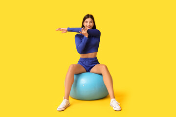 Poster - Sporty young woman sitting on fitball against yellow background