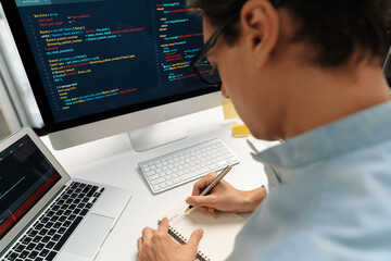 Stressful IT developer analyzing online software development information on pc and laptop with coding program on trial application project. Technical engineer writing crucial memo lists. Pecuniary.