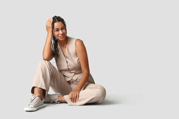 Wall Mural - Beautiful young African-American businesswoman with dreadlocks sitting on grey background