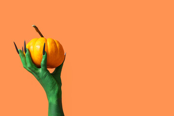 Poster - Green hand of witch with fresh pumpkin on orange background. Halloween celebration