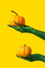 Wall Mural - Green hands of witch with fresh pumpkins on yellow background. Halloween celebration