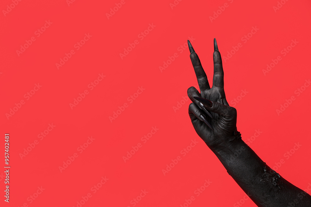 Black hand of witch showing victory gesture on red background. Halloween celebration
