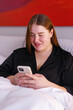 © Oleksii Syrotkin/Stocksy - Young woman in pajamas texting and smiling while sitting in her bed