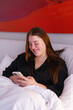 © Oleksii Syrotkin/Stocksy - Woman smiling while scrolling photos on smartphone sitting in bed