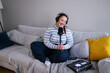 © Oleksii Syrotkin/Stocksy - Smiling plus size podcaster recording content sitting on sofa
