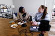 © Oleksii Syrotkin/Stocksy - Two multiracial women talking while recording podcast in living room
