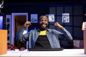 Wall Mural - Portrait of ecstatic gamer on desk chair celebrating winning videogame level in apartment. Cheerful african american player rejoicing after game victory on computer desktop