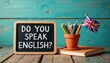 © umut hasanoglu - Chalkboard with 'Do You Speak English?' text, pencils in a pot, and British flag against a wooden background.