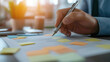 © Pimnon - A focused moment in the office, where a professional hand scribes key notes on an important document, surrounded by colorful sticky notes that capture ideas and plans in the warm daylight.