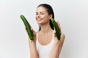 Canvas Print - Smiling woman holding cucumbers with a joyful expression, wearing a white tank top against a clean white background Fresh vegetables and healthy lifestyle concept