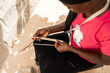 © Alvaro Lavin/Stocksy - African woman sitting and sharpening sticks for hand fan making