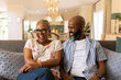 © wavebreak3 - Smiling elderly couple sitting on couch, enjoying time together at home