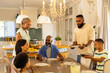 © wavebreak3 - multigenerational family gathering around dining table, serving food and enjoying meal together