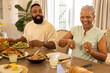 © WavebreakMediaMicro - Enjoying multigenerational family meal, smiling man and woman sitting at dining table with food