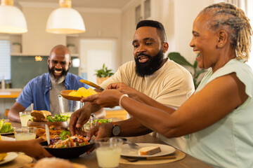 Wall Mural - multigenerational family enjoying dinner together, sharing food and laughing around dining table