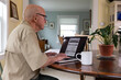 © Raymond Forbes LLC/Stocksy - Senior on computer apply Veteran Medical benefits kitchen table