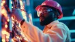 © arhendrix - Engineer in protective gear examining electrical components at an industrial facility, wearing a pink helmet and safety goggles.