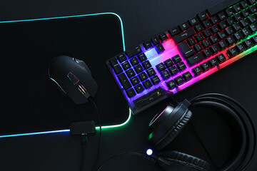 Wall Mural - Computer mouse, RGB keyboard and headset on black background, flat lay