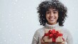 © Dai - A smiling person holding a gift box with a bright red bow, standing against an isolated snowy white background, with ample space left for adding Christmas-themed text