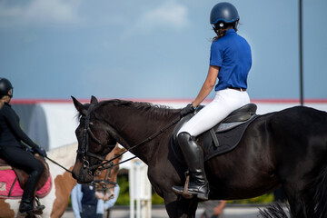 backside, teenage equestrian girl in protective helmet sits astride a horse waiting for practice rid