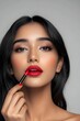 © tantawat - Beautiful Indian Woman Applying Bold Red Lipstick Glamorous Portrait with Clean Background