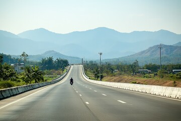 Daytime Photograph of a Large Highway in Chiang Mai Stretching into the Distance, Highlighting Expansive Road, Sharp Shadows, and Surrounding Landscape with Distant Hills Under Clear Sky