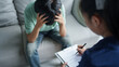 © Charlie's - sad male sitting on sofa Patient discussing mental health issues with psychologist. depressed asian man mental health treatment