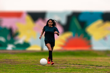 Beautiful brunette latina woman running, training and playing soccer on a green field, with colorful background, wearing sportswear, advertising and sports wellness.