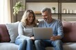 © Vooglo.com - Happy middle aged couple using laptop relaxing on couch at home.