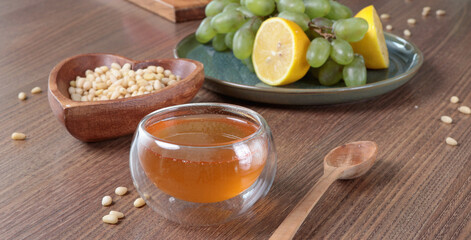 Fresh honey pour into glass bowl. Pine nuts in heart shaped plate. Wooden dishes and food on table. Useful natural food. 