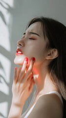 Canvas Print - A young woman with her eyes closed, touching her face with one hand. She is wearing a white tank top. Sunlight is casting shadows on her skin.