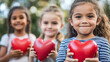 © Curva Design - happy smiling little girls looking at the camera holding red heart shape standing in the summer park outdoors  for child health day.