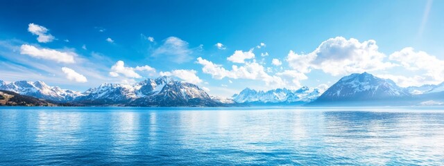 Wall Mural -  A crystal-clear body of water nestled among mountains under a vast blue sky dotted with fluffy white clouds, interspersed with a few lighter ones