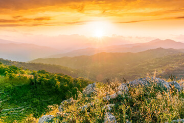 highland mountain landscape of beautiful sunset or sunrise with nice mountain peaks and slopes, green and golden hills and majestic cloudy sky on background