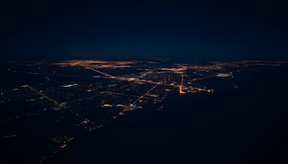 Aerial view of a coastal city at night, with a winding road and scattered lights illuminating the landscape against a dark background