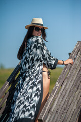 Wall Mural - beautiful girl in a black swimsuit with a hat and sunglasses on the background of the sea