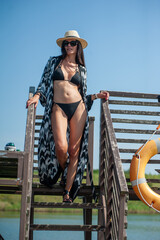 Wall Mural - beautiful girl in a black swimsuit with a hat and sunglasses on the background of the sea