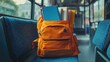 © Katty - Bright orange school backpack filled with books, resting on a bus seat, symbolizing a journey to learning.