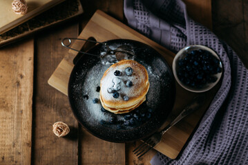 pancakes with powdered sugar, pancakes with blueberries on a dark ceramic plate on a wooden background, breakfast, holiday food