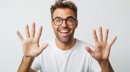 A cheerful man with glasses shows ten fingers while smiling, exuding positivity and excitement in a bright, neutral background.