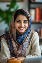 Sticker - A woman wearing a blue and brown scarf is smiling and sitting at a table with a laptop. Concept of warmth and comfort, as the woman is enjoying her time at the table