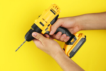 Wall Mural - Man with cordless electric drill on yellow background, closeup