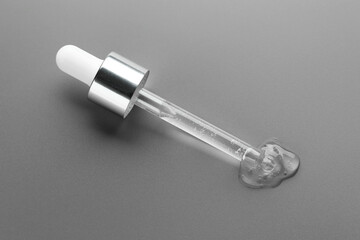 Poster - Dripping cosmetic serum from pipette on grey background, above view