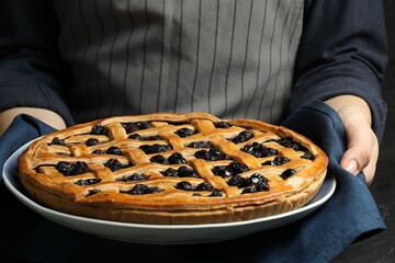 Woman holding tasty homemade pie with blueberries over table, closeup